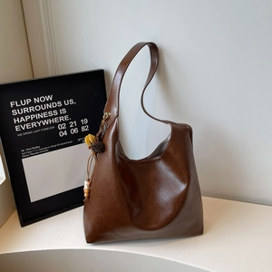Detail of large brown oil-wax leather hobo bag with ethnic pompom and bead charm