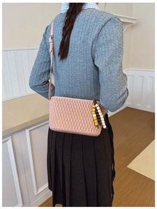 Detail of pink pleated crossbody bag with a colorful beaded pendant and slim shoulder strap
