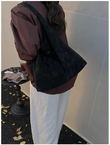 Détail d'un grand sac fourre-tout noir mat avec logo doré porté à l'épaule