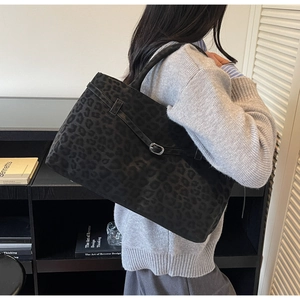 Detail of black faux suede tote bag with leopard print and decorative metal buckle