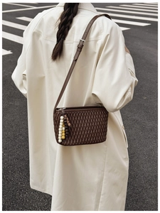 Close-up of dark brown quilted crossbody bag with colorful bead charm on a beige trench coat