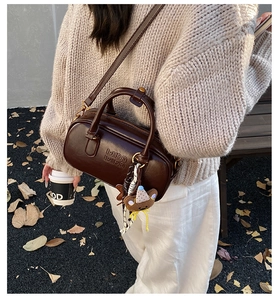 Sac Boston en cuir marron foncé avec logo embossé et breloque ours dans un décor automnal