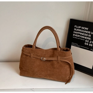 Detail of a brown suede tote bag featuring a leather strap and silver buckle on marble surface