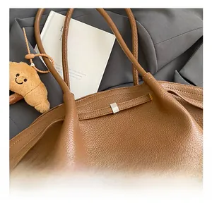 Detail shot of brown lychee grain leather handbag with silver clasp and plush croissant charm