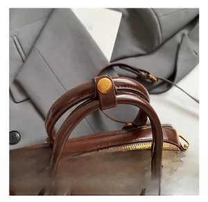 Détails d'un sac à main marron brillant avec fermeture éclair dorée et poignées rondes