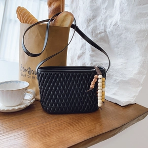 Detail of black pleated crossbody bag with stylish beaded charm on a baguette bag