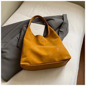 Gros plan du sac en cuir mat jaune moutarde avec logo métallique sur un blazer gris
