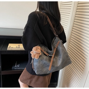 Detail shot of a dark grey tote bag with brown leather straps and a plush bear charm