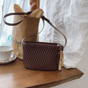 Close-up of dark brown woven handbag with wooden bead tassel charm on a wooden table