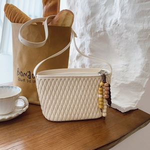 Detail of quilted cream crossbody bag featuring a unique wooden bead tassel decoration