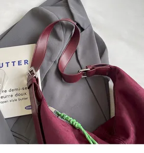 Detail of burgundy suede hobo bag featuring green woven rope zipper pull and silver buckle