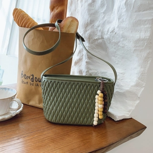 Detail of green quilted PU leather crossbody bag with wooden bead charm on a wooden table
