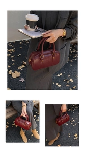 Detailed close-up of a burgundy leather Boston bag with metallic gold zipper and handles