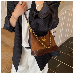 Detail of a brown quilted leather crossbody bag with chain and velvet splicing on model