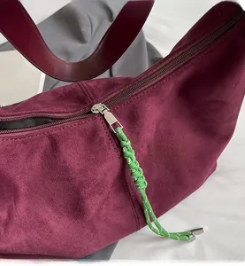 Close-up of smooth metal zipper on burgundy suede tote bag with green cord puller