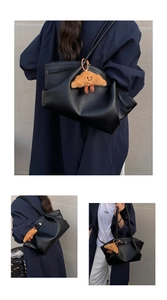 Detail of black lychee grain leather tote bag with a cute plush croissant charm pendant