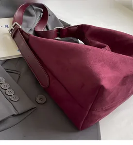 Detail view of burgundy suede shoulder bag with silver buckle on grey suit jacket