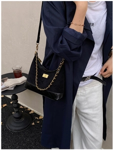 Detail of black quilted hobo bag featuring a gold square twist lock and metal chain strap