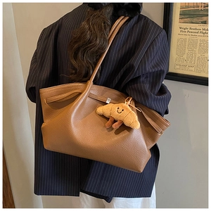 Detail view of brown lychee grain leather tote bag featuring a cute croissant plush pendant