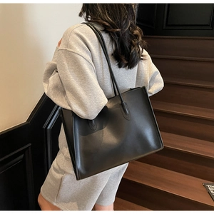 Detail of black large capacity tote bag in smooth PU leather held by a model on stairs