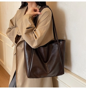 Detailed view of large dark brown leather tote bag worn with a beige trench coat
