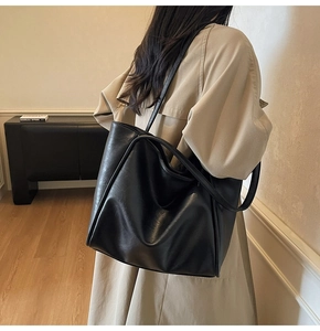 Minimalist black faux leather tote bag shown on model with chic beige trench coat