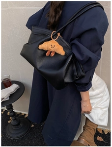 Detail of black lychee grain leather tote bag with a cute plush croissant charm pendant