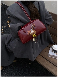 Deep red patent leather bowling bag with cute brown bear charm on outdoor bench