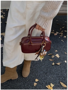 Détail du sac Boston bordeaux avec logo embossé et charm ours dans un cadre extérieur