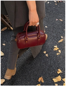 Close-up of a burgundy leather Boston bag with Mira Mira embossing in a street scene