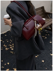 Detail view of burgundy leather bowling bag with cute teddy bear charm on model shoulder