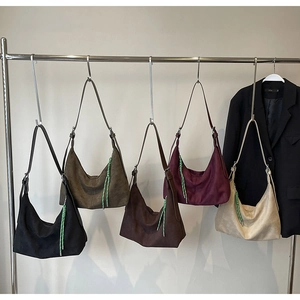 Detail view showing five colorful suede tote bags with woven charms on a metal rack