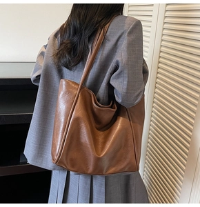 Rear view of a large brown leather tote bag worn by a model in a stylish office setting