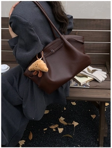 Detail of dark brown lychee leather tote bag with a cute croissant plush charm pendant