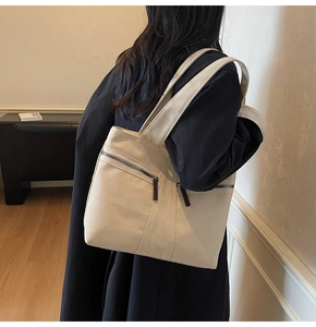 Model wearing a large cream canvas tote bag with side zippers in a minimalist room