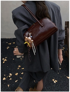Detail of burgundy leather bowling bag with cute teddy bear charm and sleek shoulder straps