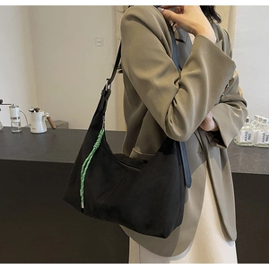 Detail of a black large Hobo shoulder bag with a green woven strap on a model's shoulder