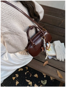 Sac à main cylindrique en cuir marron avec breloques dans un décor d'automne