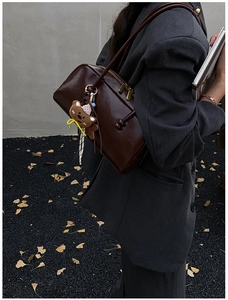 Detail of dark brown leather bowling bag with gold zipper and bear charm accessory