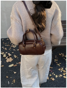 Detail view of the deep coffee patent leather cylinder bag with gold hardware on a model