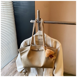 Close-up of beige lychee grain leather tote bag with a cute plush croissant charm detail