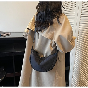 Detail showing a black crescent crossbody bag on a model wearing a trench coat