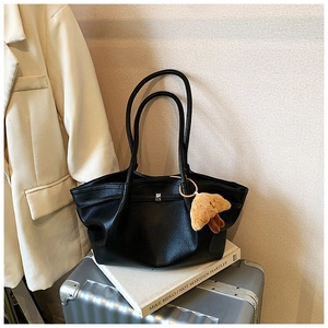 Detail of black lychee grain tote bag with a plush croissant charm on a silver suitcase