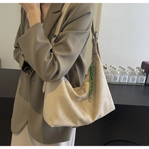 Detail of beige suede hobo bag with green braided rope charm on model shoulder