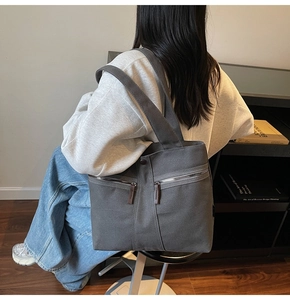Deep grey canvas tote bag with front metal zippers shown on shoulder in lifestyle setting