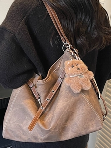 Brown vintage tote bag with contrast stitching and plush bear charm worn by a model