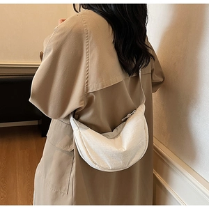 White crescent dumpling bag shown on shoulder of a woman wearing a khaki trench coat