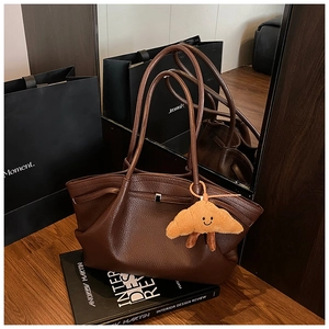 Macro detail of dark brown lychee leather texture on tote bag with plush charm