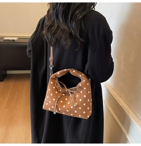 Sac à main en daim marron à pois blancs avec détail de nœud porté par le mannequin
