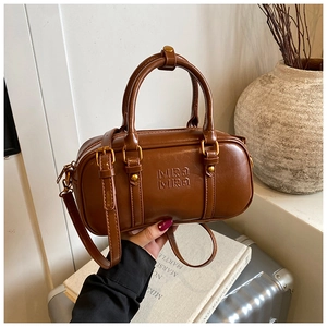 Detail of retro mini Boston bag in caramel brown leather with embossed logo and golden hardware